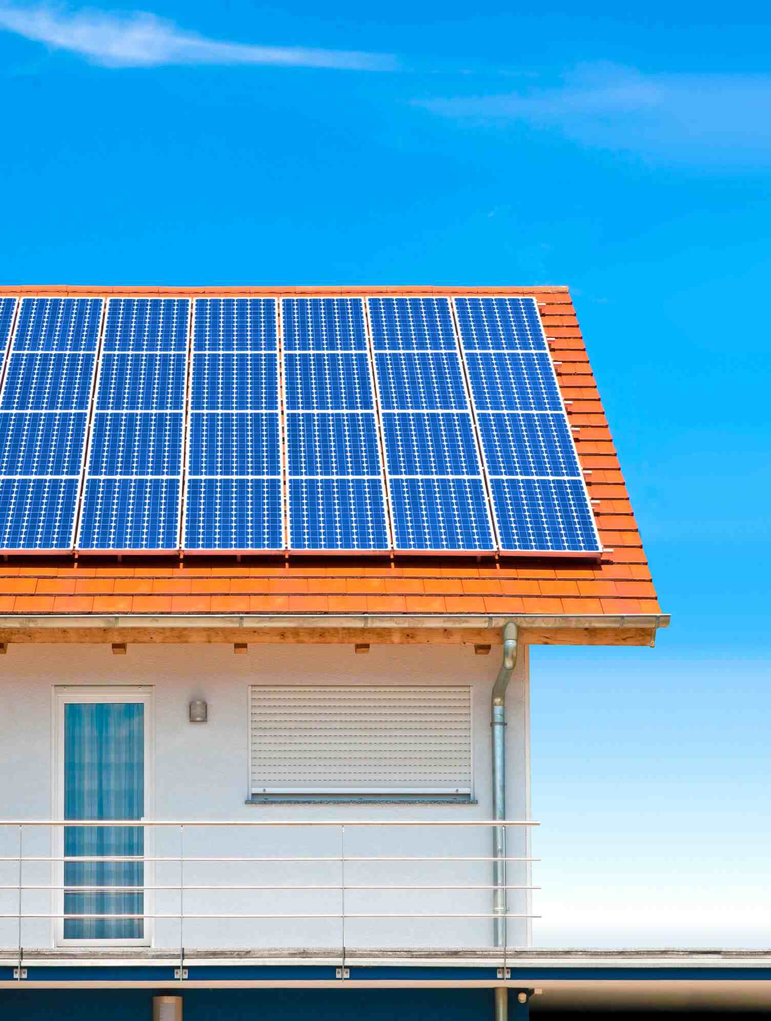 Blue solar panels installed on red tile roof of modern house against clear blue sky