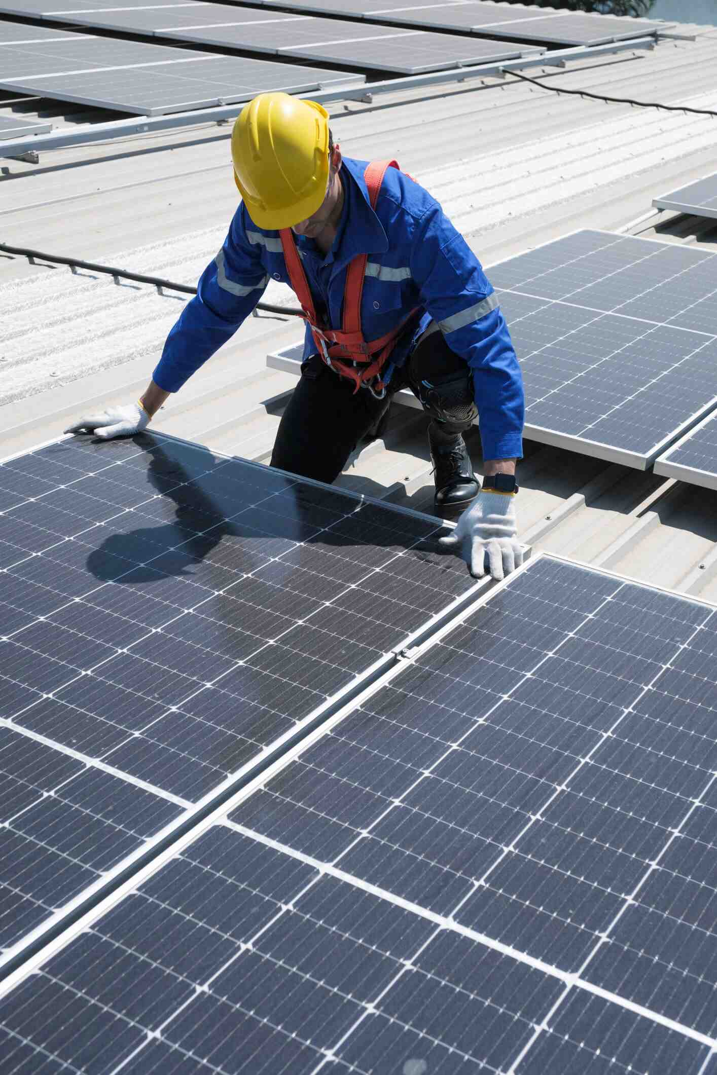 Solar panel technician in yellow hard hat installing photovoltaic panels on roof