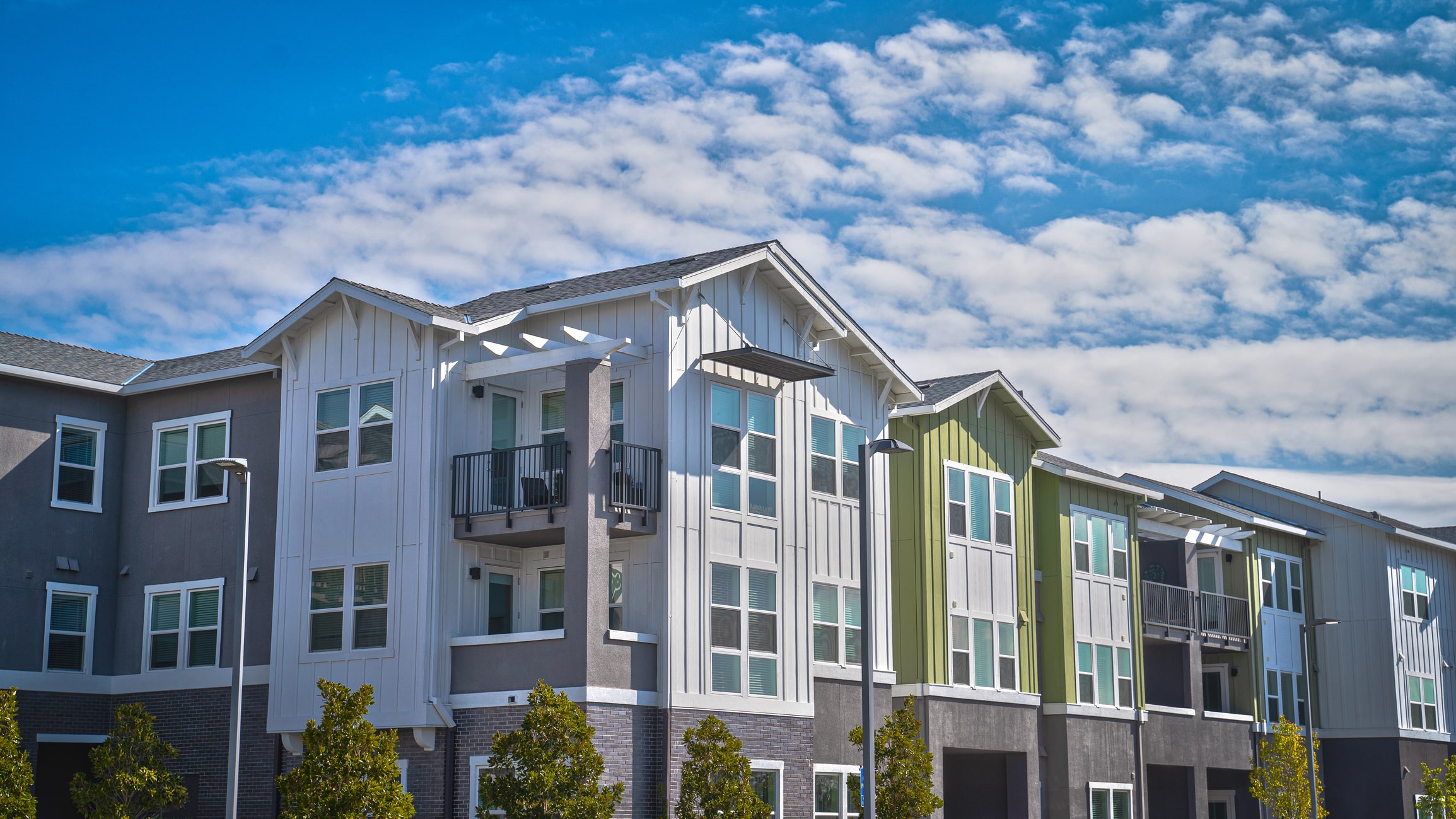Modern townhouses with colorful siding and balconies under blue sky with clouds